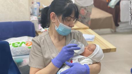 Uma babá em uma clínica de barriga de aluguel alimenta um bebê recém-nascido esperando para ser pego por seus novos pais.