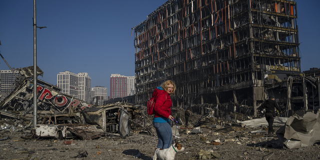 Irina Zubchenko passeia com seu cachorro Max em meio à devastação causada pelo bombardeio de um shopping center em Kiev, na Ucrânia, na segunda-feira.