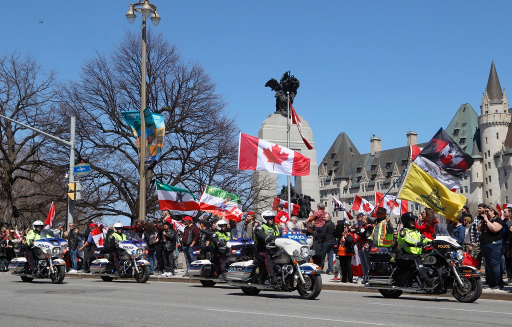 Policiais em motocicletas passam por uma manifestação, parte de uma demonstração ao estilo de um comboio "trovão rolando" Em Ottawa, Ontário, no sábado, 30 de abril de 2022.