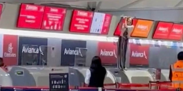 Outros passageiros no aeroporto podem ver a pessoa fora de controle - de pé no balcão de check-in e segurando uma tela sobre ele - de longe.