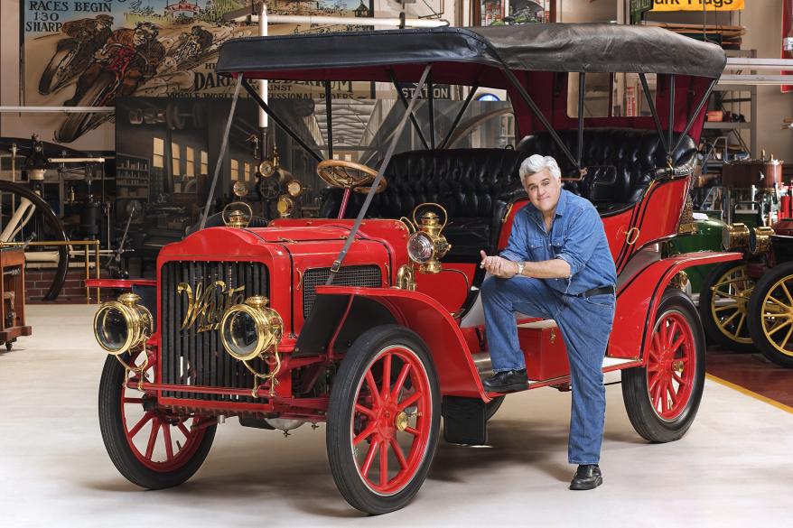 Foto de Jay Leno parado na frente de seu carro.