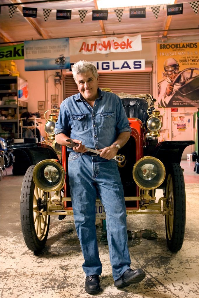 Foto de Jay Leno parado na frente de seu carro.